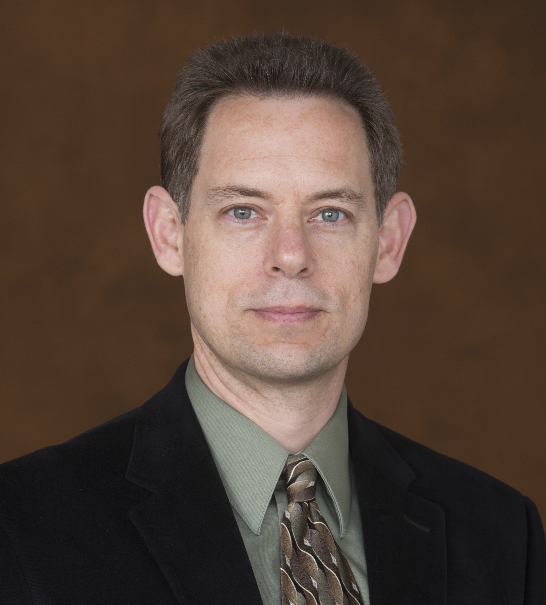 Greg Siering poses for a headshot. He wears a blazer and tie.