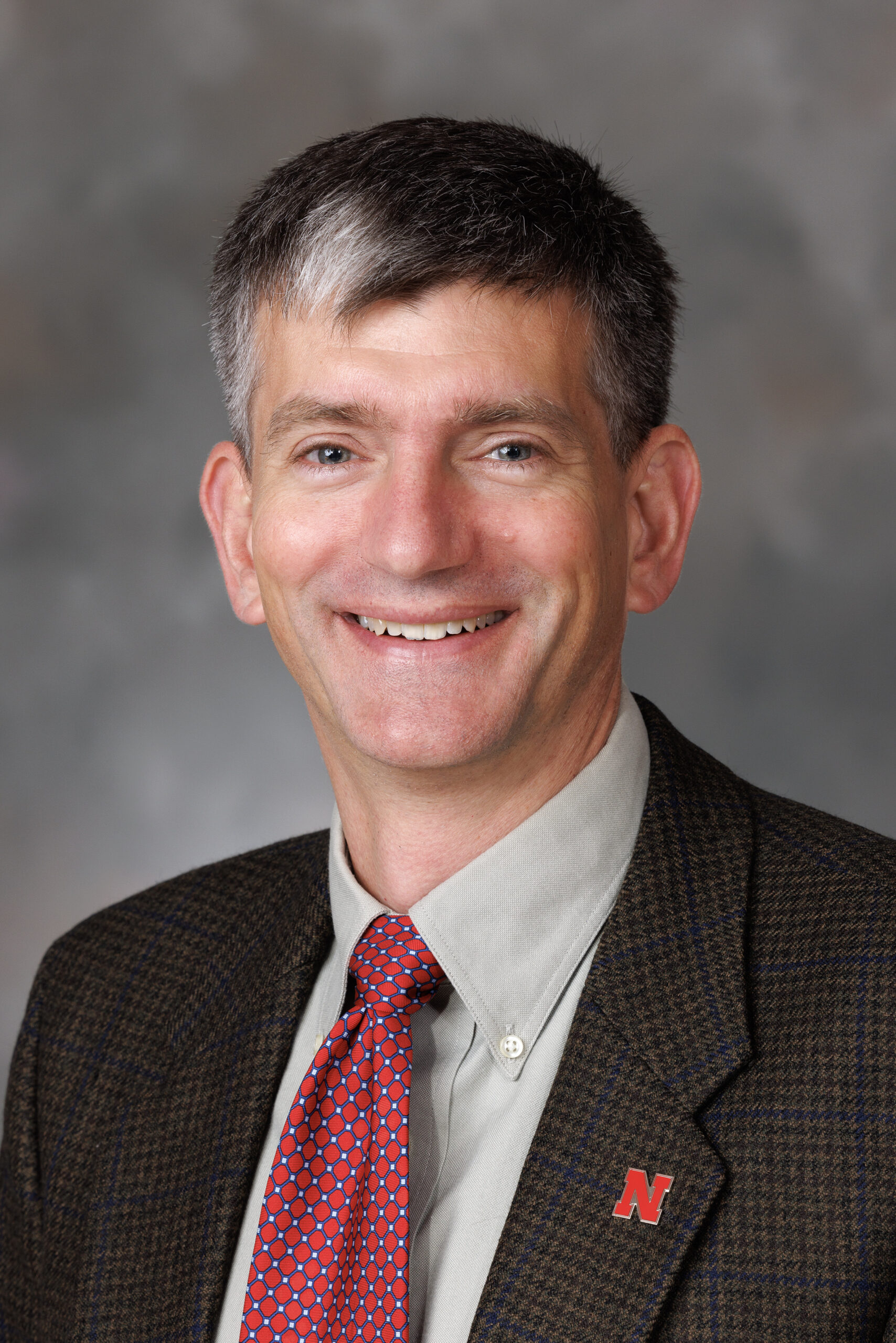 Greg Siering poses for a headshot. He wears a blazer and tie.